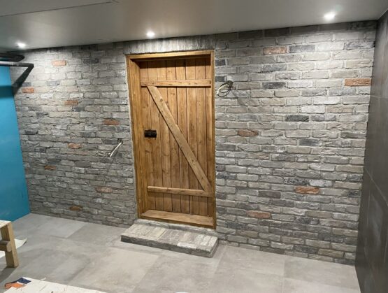 Remontoitu kellarihuone, jossa on maalaismainen puuovi ja koristeellinen tiilipinta seinässä